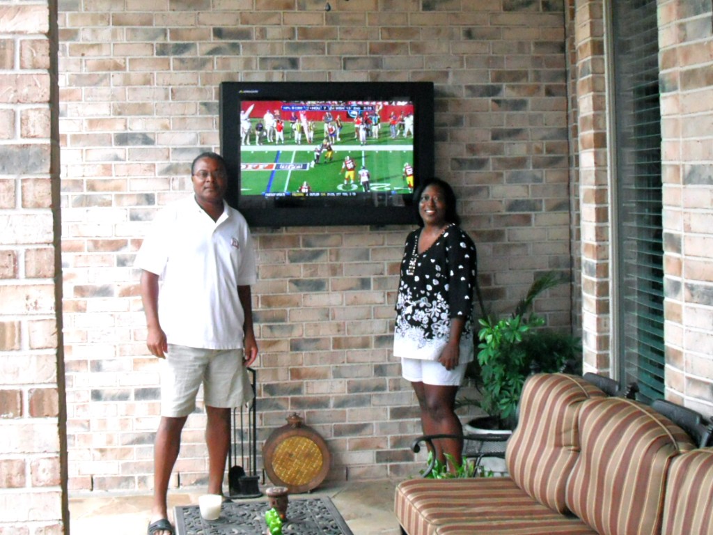 a man and a lady standing next to an outdoor screen with an LCD TV Protection enclosure